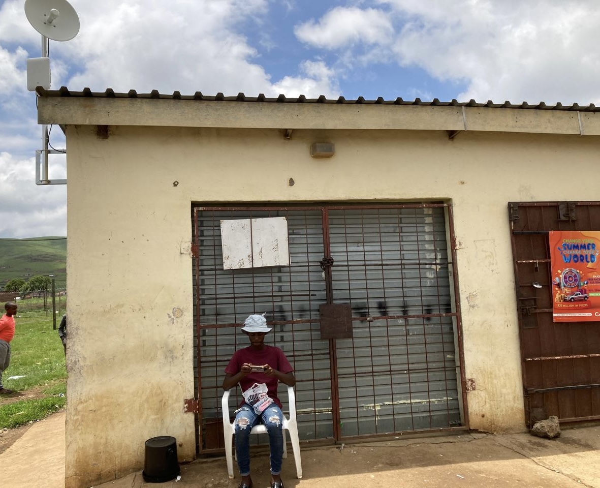 A community hotspot antenna mounted above a small container shop in South Africa, with local residents gathered outside